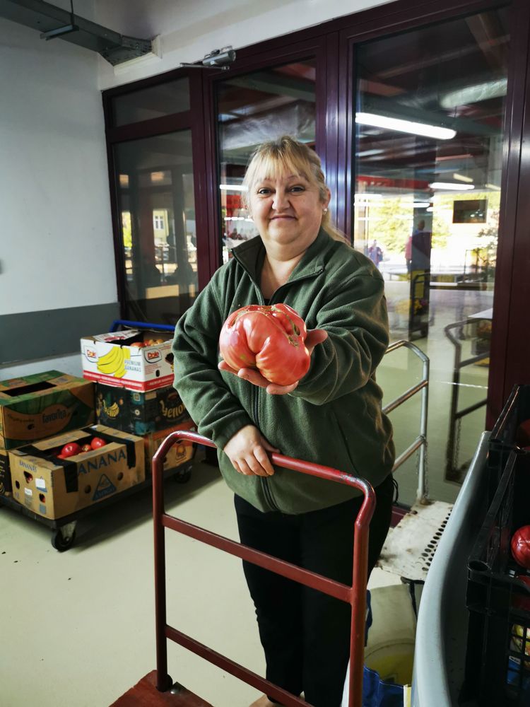 Market lady shows a tomato the size of a head.
