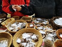 People look at seed packets lying in various baskets and trays on a table.