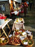 Ein Marktstand im Freien mit Körben voller Äpfel und Tischen mit Apfelprodukten. Personen im Hintergrund betrachten die Waren.